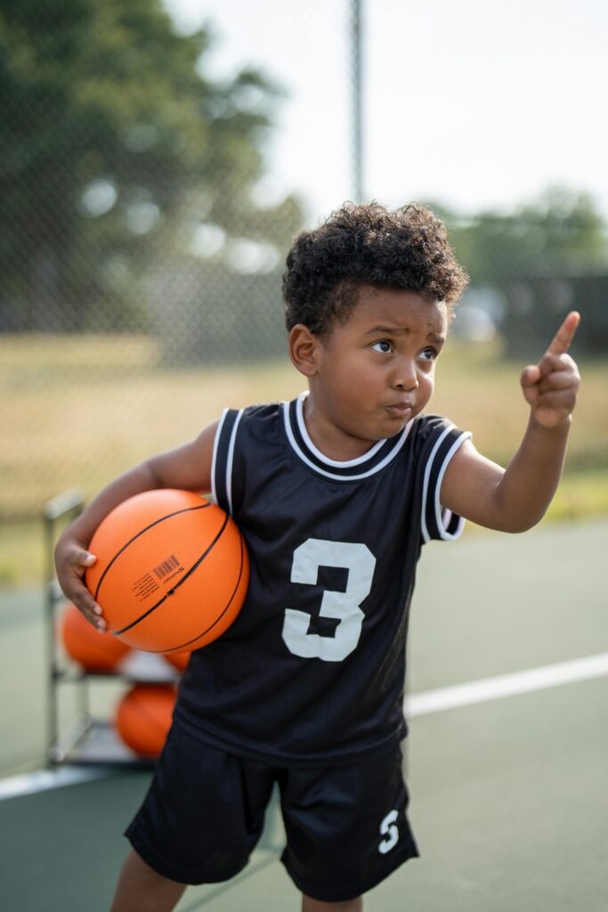 pexels-photo-30637225-30637225 A young boy holding a basketball on an outdoor court, pointing energetically.